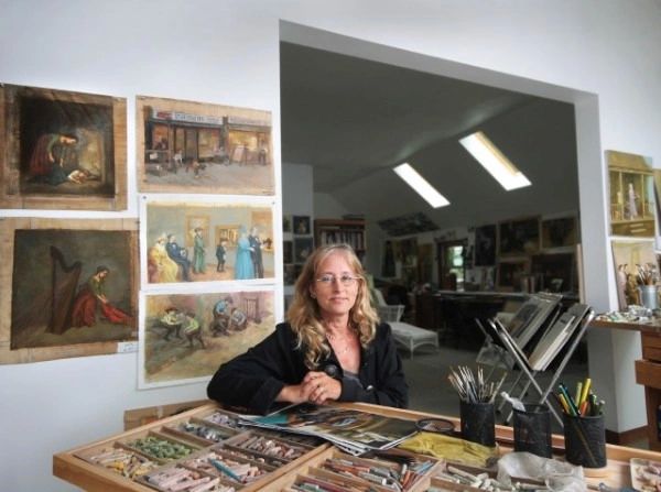 A woman sitting at a table in front of paintings.